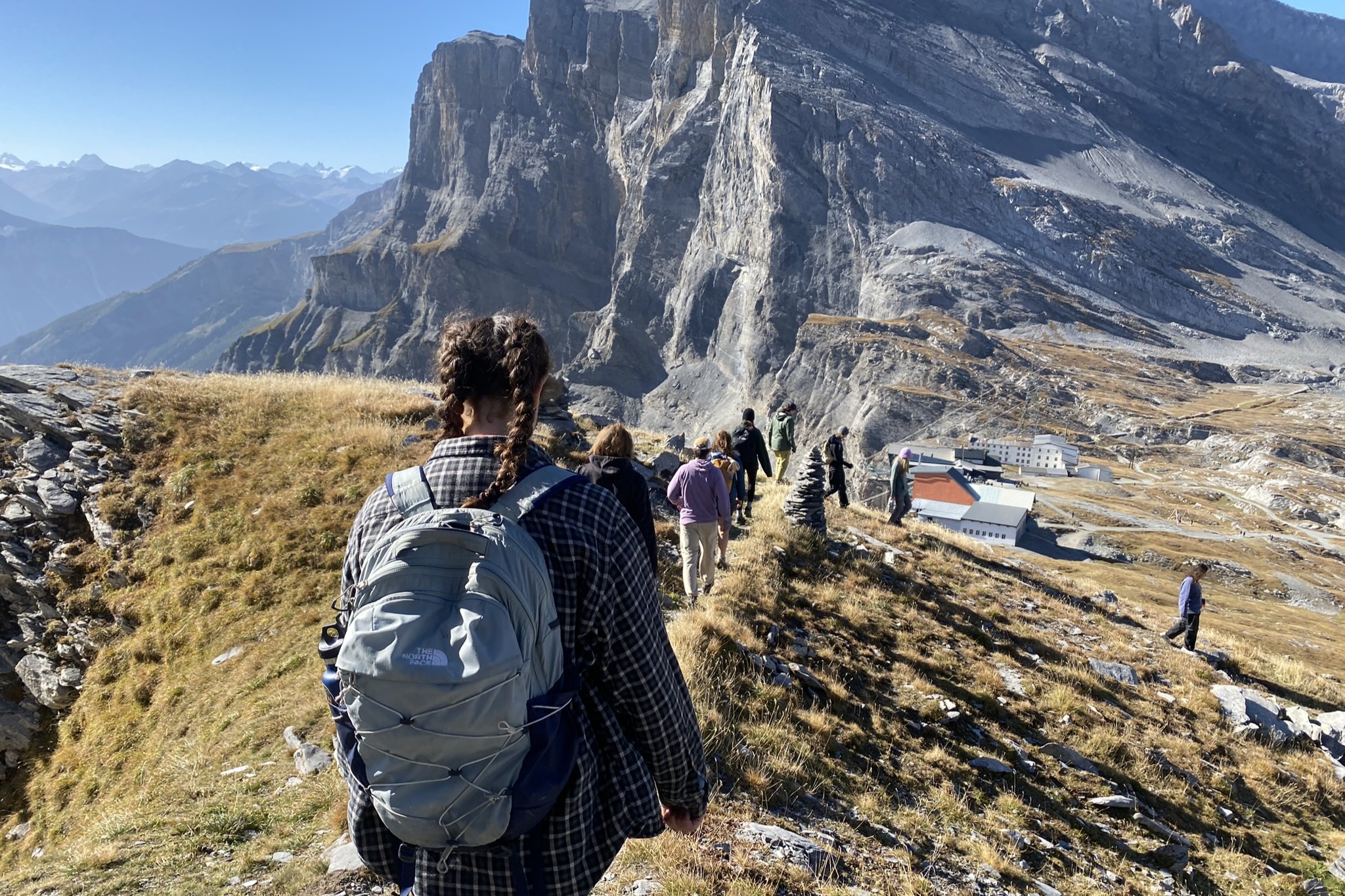 A line of students traverse a mountain in the Swiss Alps, wearing backpacks.